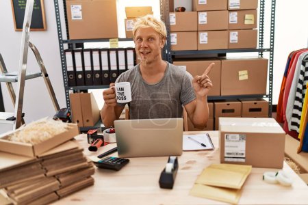 Téléchargez les photos : Jeune homme blond buvant du café travaillant à la boutique en ligne souriant heureux pointant avec la main et le doigt sur le côté - en image libre de droit