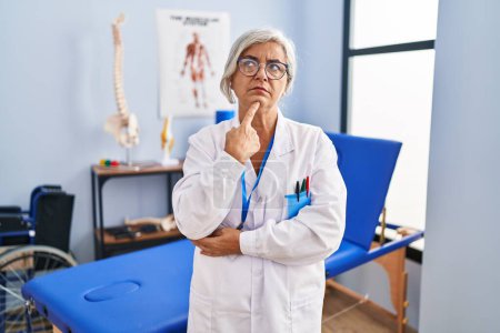 Photo for Middle age woman with grey hair working at pain recovery clinic thinking concentrated about doubt with finger on chin and looking up wondering - Royalty Free Image