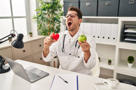 Photo for Young hispanic man working at dietitian clinic angry and mad screaming frustrated and furious, shouting with anger. rage and aggressive concept. - Royalty Free Image