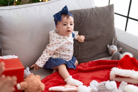 Photo for Adorable toddler sitting on sofa by christmas tree at home - Royalty Free Image