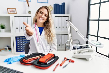 Photo for Young beautiful doctor woman with reflex hammer and medical instruments smiling friendly offering handshake as greeting and welcoming. successful business. - Royalty Free Image