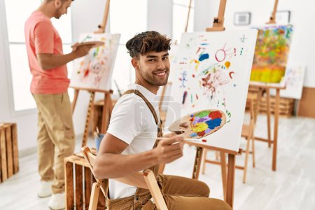 Téléchargez les photos : Deux hommes hispaniques couple souriant dessin confiant au studio d'art - en image libre de droit