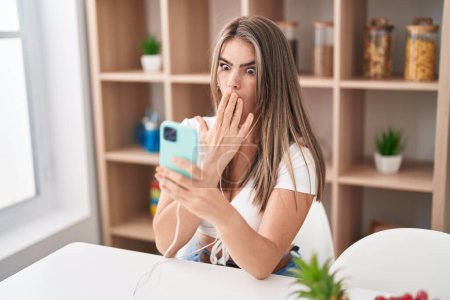 Photo for Young beautiful woman doing video call with smartphone covering mouth with hand, shocked and afraid for mistake. surprised expression - Royalty Free Image