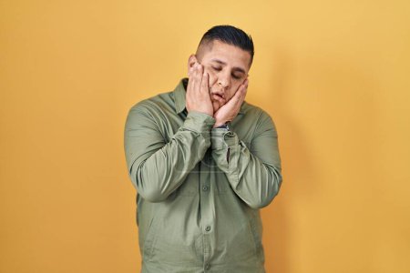 Téléchargez les photos : Jeune homme hispanique debout sur fond jaune mains fatiguées couvrant le visage, la dépression et la tristesse, contrarié et irrité par le problème - en image libre de droit