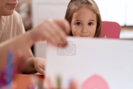 Téléchargez les photos : Adorable étudiante hispanique assise sur une table de papier à découper à la maternelle - en image libre de droit
