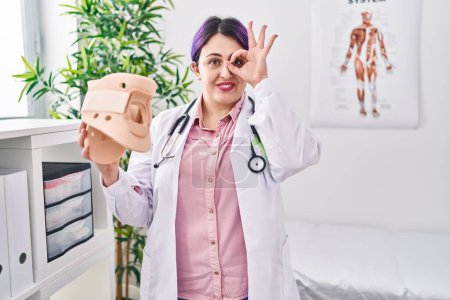 Photo for Plus size doctor woman wit purple hair holding cervical neck collar smiling happy doing ok sign with hand on eye looking through fingers - Royalty Free Image
