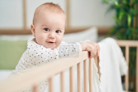 Téléchargez les photos : Adorable bébé caucasien souriant confiant debout sur le berceau à la chambre - en image libre de droit
