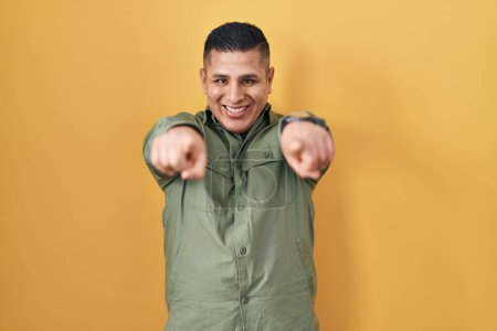 Téléchargez les photos : Jeune homme hispanique debout sur fond jaune pointant vers vous et la caméra avec les doigts, souriant positif et joyeux - en image libre de droit