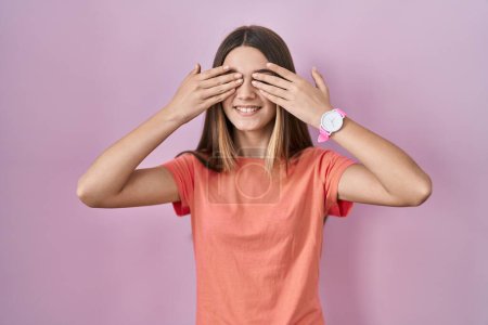 Téléchargez les photos : Teenager girl standing over pink background covering eyes with hands smiling cheerful and funny. blind concept. - en image libre de droit