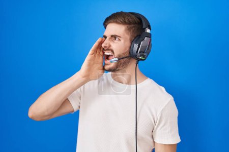 Téléchargez les photos : Hispanic man with beard listening to music wearing headphones shouting and screaming loud to side with hand on mouth. communication concept. - en image libre de droit
