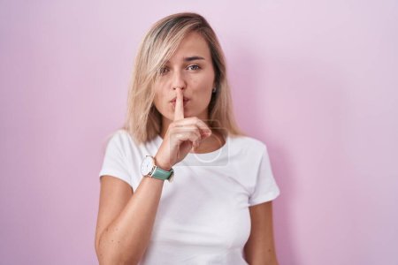 Téléchargez les photos : Young blonde woman standing over pink background asking to be quiet with finger on lips. silence and secret concept. - en image libre de droit