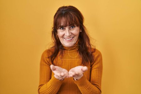 Téléchargez les photos : Middle age hispanic woman standing over yellow background smiling with hands palms together receiving or giving gesture. hold and protection - en image libre de droit