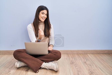 Photo for Young brunette woman working using computer laptop sitting on the floor beckoning come here gesture with hand inviting welcoming happy and smiling - Royalty Free Image
