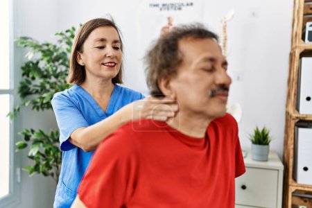 Photo for Middle age man and woman wearing physiotherapy uniform having rehab session massaging neck at physiotherapy clinic - Royalty Free Image