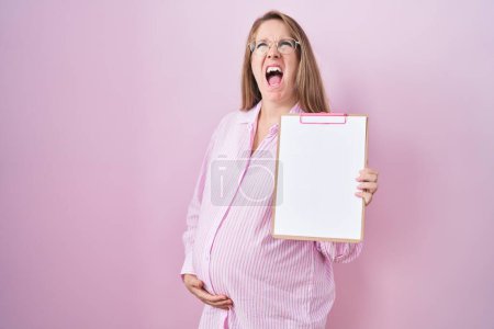 Téléchargez les photos : Jeune femme enceinte tenant presse-papiers en colère et fou hurlant frustré et furieux, criant de colère levant les yeux. - en image libre de droit