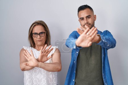 Photo for Hispanic mother and son standing together rejection expression crossing arms and palms doing negative sign, angry face - Royalty Free Image
