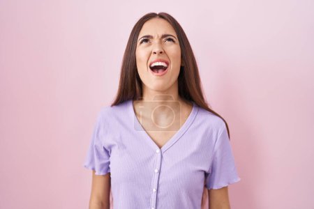 Téléchargez les photos : Young hispanic woman with long hair standing over pink background angry and mad screaming frustrated and furious, shouting with anger. rage and aggressive concept. - en image libre de droit
