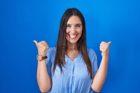 Téléchargez les photos : Jeune femme brune debout sur fond bleu signe de succès faire un geste positif avec la main, pouces levés souriant et heureux. expression joyeuse et geste gagnant. - en image libre de droit