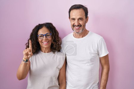 Téléchargez les photos : Middle age hispanic couple together over pink background showing and pointing up with finger number one while smiling confident and happy. - en image libre de droit