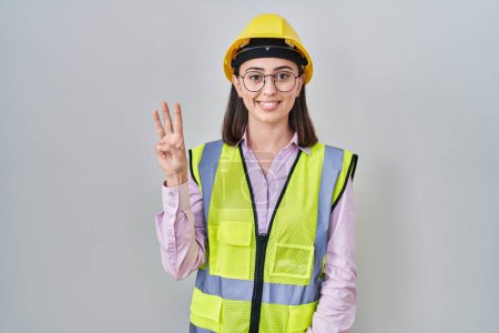 Photo for Hispanic girl wearing builder uniform and hardhat showing and pointing up with fingers number three while smiling confident and happy. - Royalty Free Image
