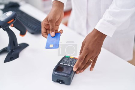 Photo for Middle age african american woman pharmacist using credit card and data phone at pharmacy - Royalty Free Image