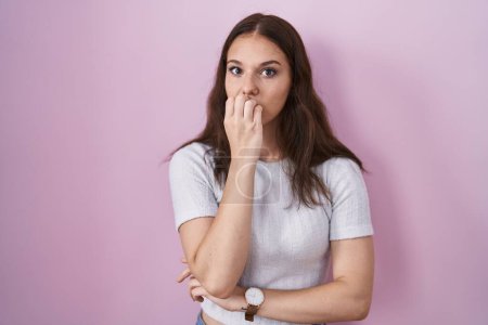 Foto de Young hispanic girl standing over pink background looking stressed and nervous with hands on mouth biting nails. anxiety problem. - Imagen libre de derechos