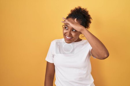 Photo for Young hispanic woman with curly hair standing over yellow background very happy and smiling looking far away with hand over head. searching concept. - Royalty Free Image