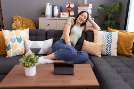 Téléchargez les photos : Young beautiful woman watching video on touchpad sitting on sofa at home - en image libre de droit