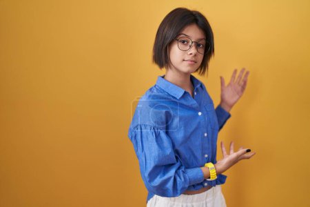 Foto de Young girl standing over yellow background inviting to enter smiling natural with open hand - Imagen libre de derechos