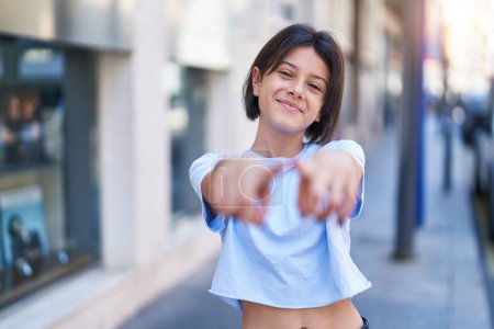 Adorable hispanic girl smiling confident pointing with fingers to the camera at street