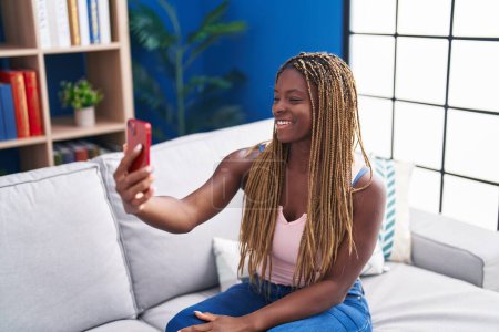 Téléchargez les photos : Femme afro-américaine faire selfie par smartphone assis sur le canapé à la maison - en image libre de droit