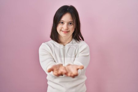 Téléchargez les photos : Woman with down syndrome standing over pink background smiling with hands palms together receiving or giving gesture. hold and protection - en image libre de droit