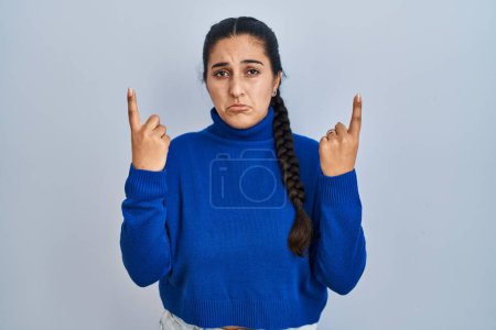 Téléchargez les photos : Jeune femme hispanique debout sur fond isolé pointant vers le haut regardant triste et contrarié, indiquant la direction avec les doigts, malheureux et déprimé. - en image libre de droit
