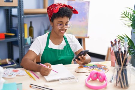 Téléchargez les photos : Artiste afro-américaine utilisant un smartphone dessin sur ordinateur portable au studio d'art - en image libre de droit