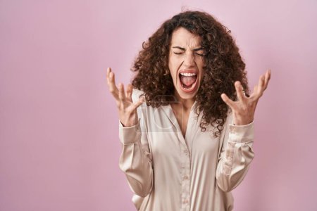 Téléchargez les photos : Hispanic woman with curly hair standing over pink background celebrating mad and crazy for success with arms raised and closed eyes screaming excited. winner concept - en image libre de droit