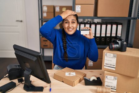 Foto de Mujer hispana joven que trabaja en el comercio electrónico de pequeñas empresas con tarjeta de crédito estresada y frustrada con la mano en la cabeza, cara sorprendida y enojada - Imagen libre de derechos