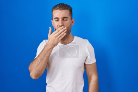 Téléchargez les photos : Young caucasian man standing over blue background bored yawning tired covering mouth with hand. restless and sleepiness. - en image libre de droit