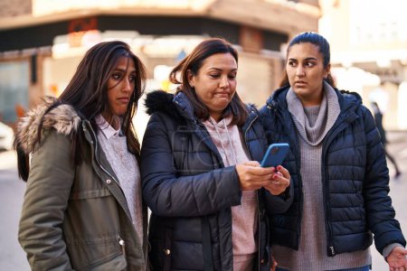 Photo for Three woman mother and daughters using smartphone at street - Royalty Free Image