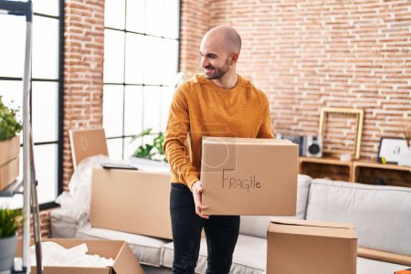 Photo for Young man smiling confident holding fragile cardboard box at new home - Royalty Free Image