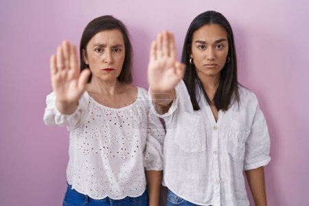 Photo for Hispanic mother and daughter together doing stop sing with palm of the hand. warning expression with negative and serious gesture on the face. - Royalty Free Image