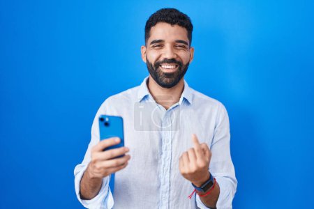 Photo for Hispanic man with beard using smartphone typing message beckoning come here gesture with hand inviting welcoming happy and smiling - Royalty Free Image
