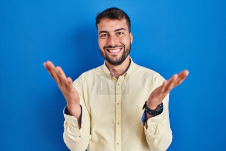 Téléchargez les photos : Bel homme hispanique debout sur fond bleu souriant joyeux offrant mains donnant assistance et acceptation. - en image libre de droit