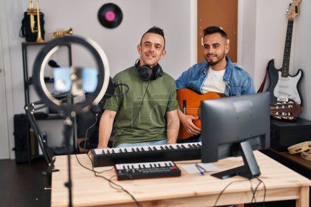Téléchargez les photos : Deux hommes jouant de la guitare classique au studio de musique enregistrant la chanson regardant positif et heureux debout et souriant avec un sourire confiant montrant des dents - en image libre de droit