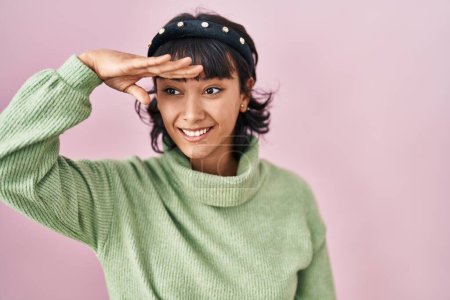 Foto de Young beautiful woman standing over pink background very happy and smiling looking far away with hand over head. searching concept. - Imagen libre de derechos