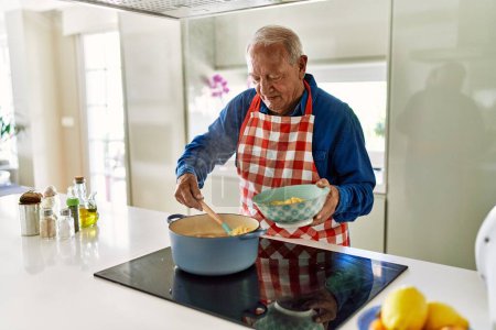 Foto de Hombre mayor sonriendo confiado cocinando espaguetis en la cocina - Imagen libre de derechos
