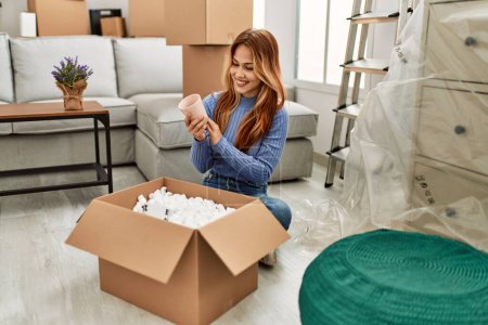 Téléchargez les photos : Young caucasian woman smiling confident unpacking cardboard box at new home - en image libre de droit