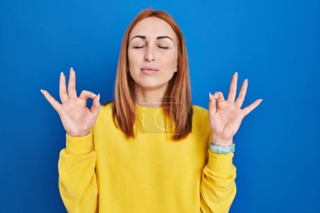 Téléchargez les photos : Young woman standing over blue background relaxed and smiling with eyes closed doing meditation gesture with fingers. yoga concept. - en image libre de droit