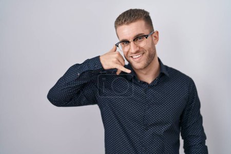 Téléchargez les photos : Jeune homme caucasien debout sur fond isolé souriant faire geste de téléphone avec la main et les doigts comme parler au téléphone. communiquer les concepts. - en image libre de droit