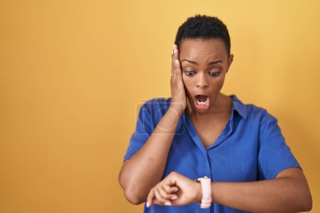Foto de African american woman standing over yellow background looking at the watch time worried, afraid of getting late - Imagen libre de derechos