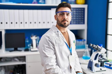 Photo for Young hispanic man wearing scientist uniform with serious expression at laboratory - Royalty Free Image